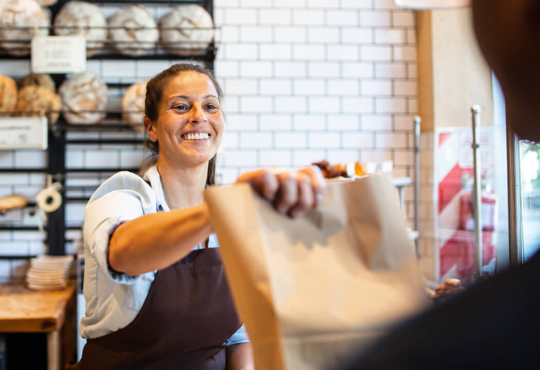 woman handing over a brown bag in a bakery 